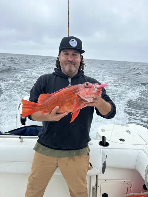 Captain holding a bright red vermilion rockfish in the cockpit underway.
