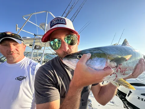 Two anglers in sunglasses holding a yellowtail aboard the boat.