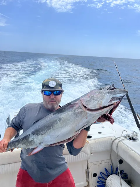 Captain holding a bluefin tuna in the cockpit with the wake trailing behind.