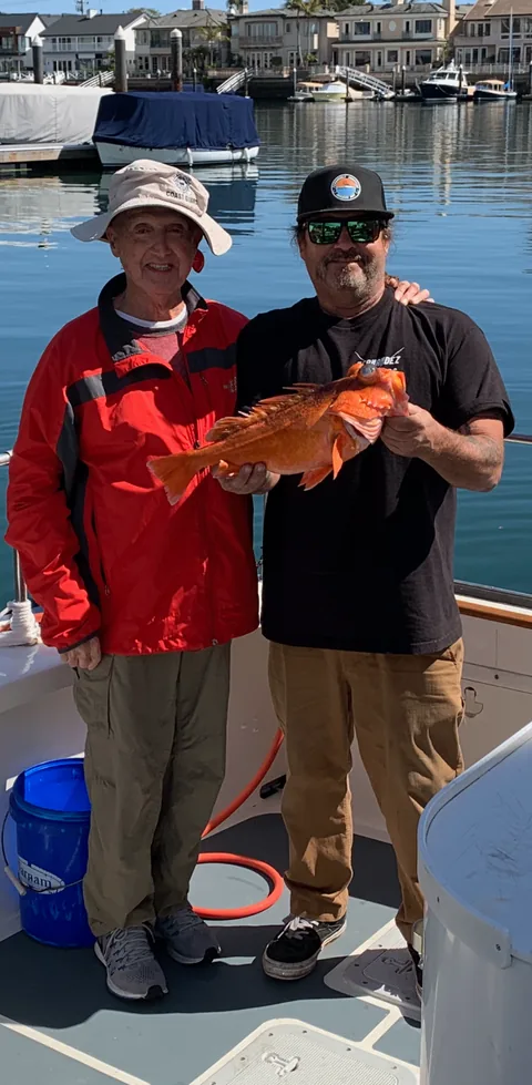 Two anglers holding a bright orange vermilion rockfish at the dock in Mission Bay.