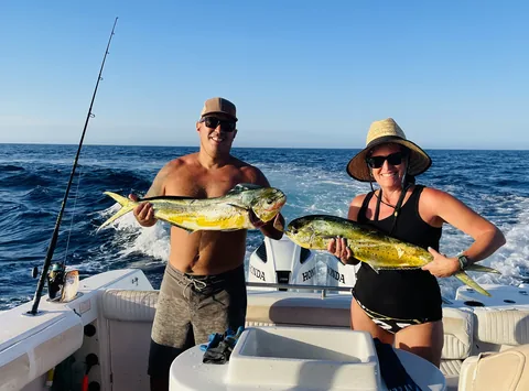 Two guests each holding a golden dorado on the deck offshore.