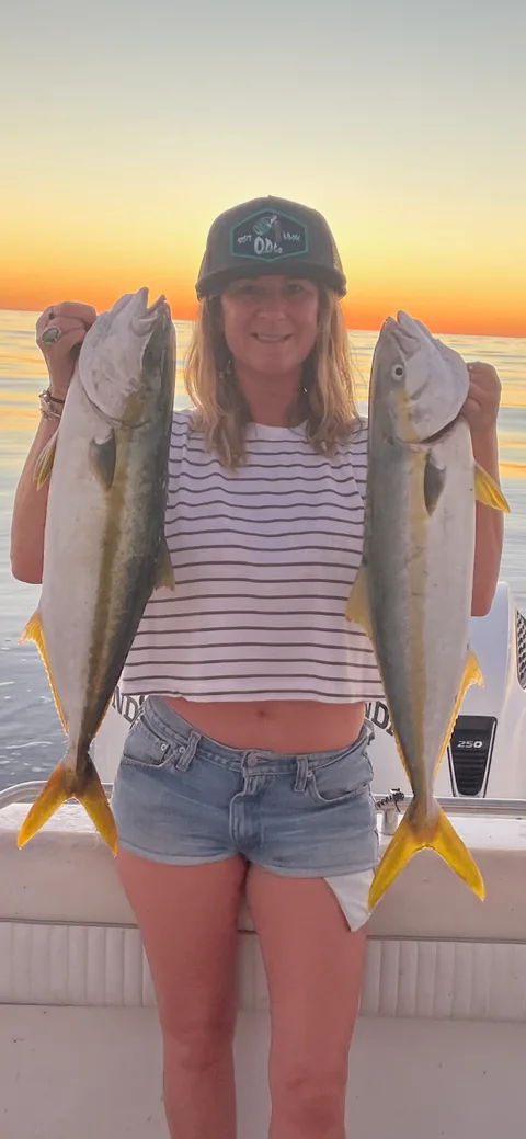 Angler holding two yellowtail at sunset on flat offshore water.