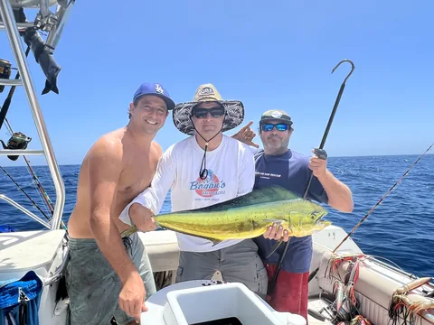 Three anglers smiling with a dorado offshore under blue skies.