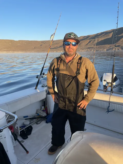 Captain standing in the cockpit with trolling rods out and the island behind at sunset.